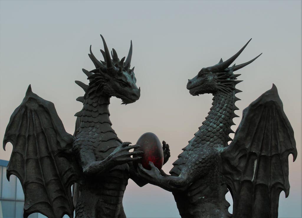 Two impressive dragon sculptures holding an enigmatic egg against a twilight sky, symbolizing fantasy and myth.