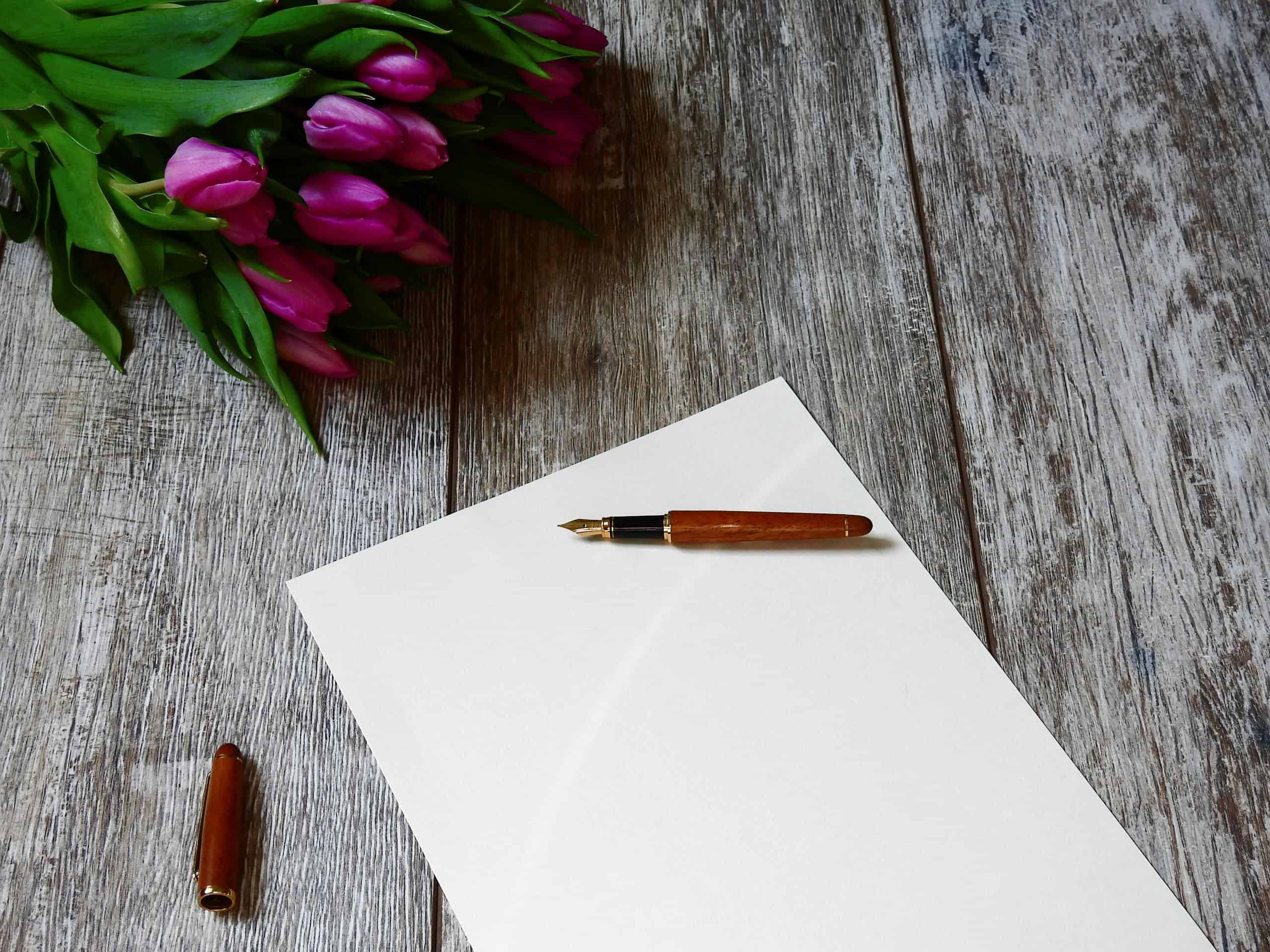 A blank note with a fountain pen and purple tulips on a wooden table, ideal for creating campaigns.