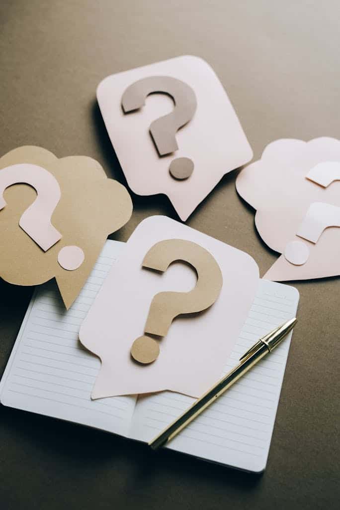 Artistic paper question marks on an open notebook with a pen, symbolizing curiosity and creativity.