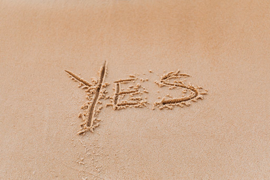 The word 'YES' artistically written on warm beach sand, capturing a moment of positivity and simplicity.