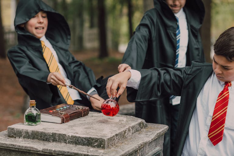 Three children in wizard costumes play with potions and wands in a fantasy-themed setting outdoors.