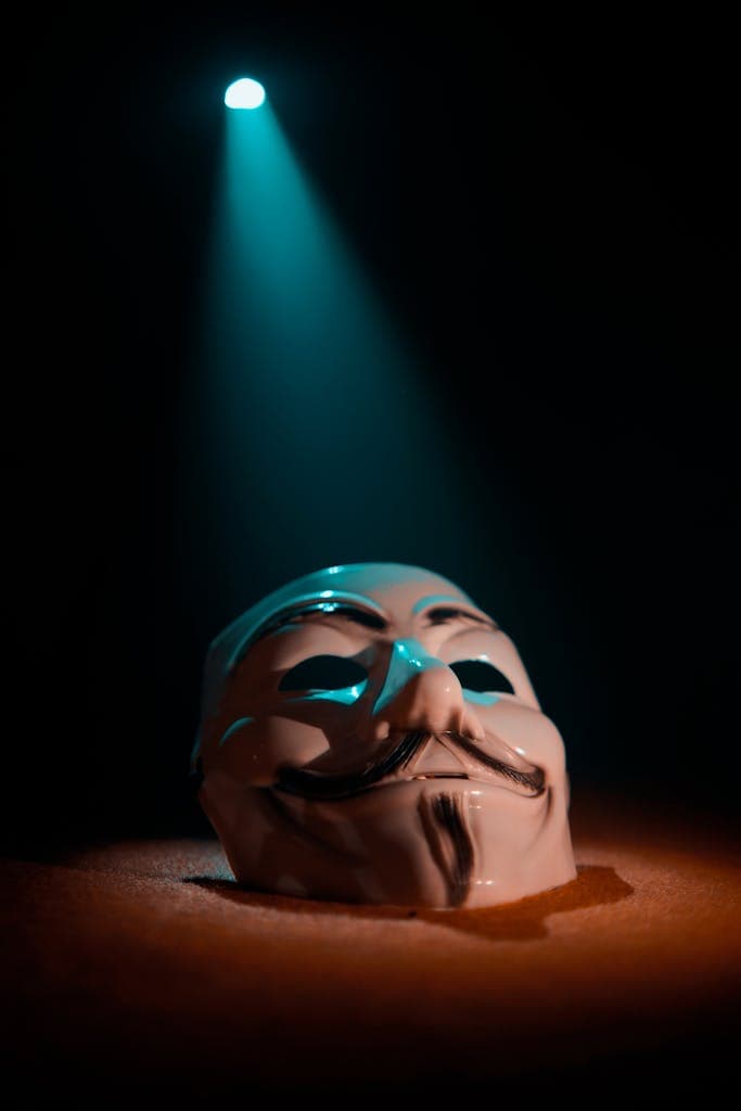 A close-up of a white anonymous mask under a dramatic teal spotlight on a dark background.